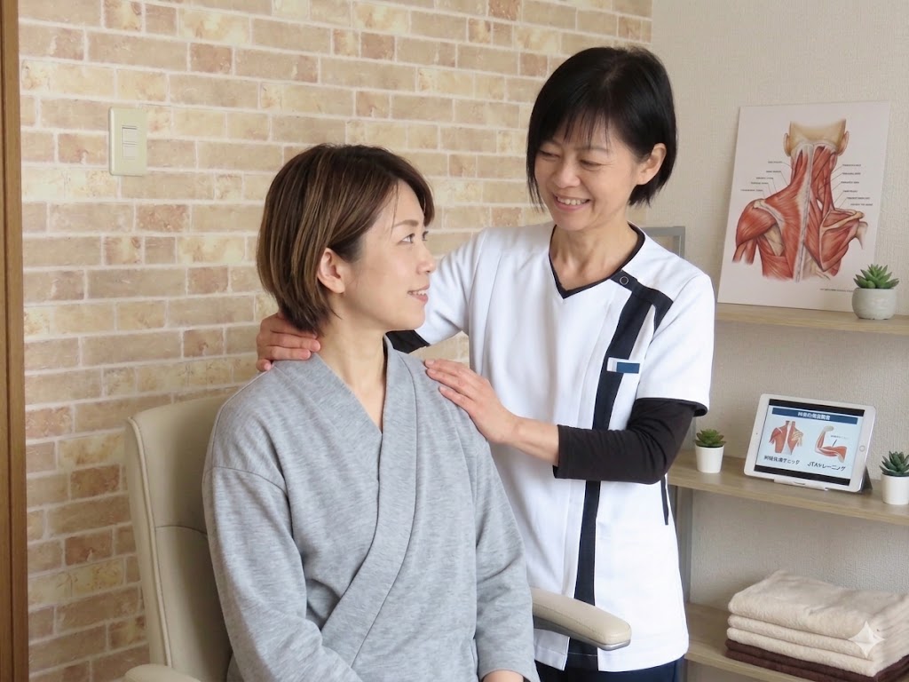 仙台市長町の整体院dolmilでの施術風景。神経整体とJTAに基づき、座った姿勢で首や肩の筋肉を調整するセラピストの野口。背景には解剖図のパネルが置かれ、専門的な治療環境を示している。